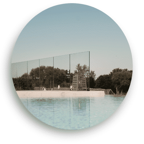 Glasräcke utan stolpar monterat vid en pool, skapar en vindskyddad yta med fri utsikt över omgivningen. Klart säkerhetsglas ger en diskret och exklusiv inramning av poolområdet.