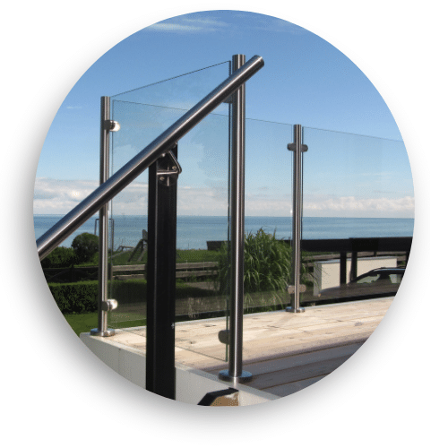Moderne glassgjerde med rustfrie stolper og håndløper montert på terrasse med åpen utsikt mot havet.