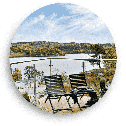 Glasräcke med rostfria stolpar monterat på en träterrass med utsikt över en sjö. Två solstolar står placerade mot räcket, vilket skapar en inbjudande plats att njuta av utsikten.