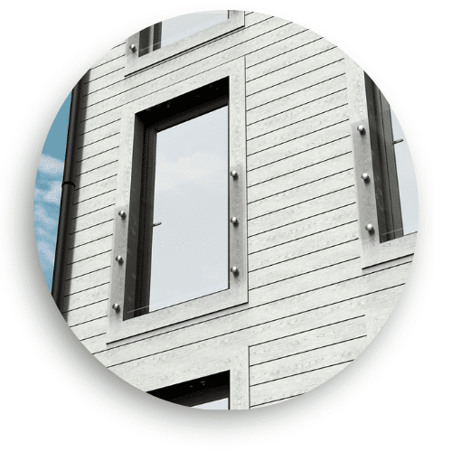 Détail de balcon avec verre monté sur façade moderne en bois gris, avec fixations apparentes et design industriel.