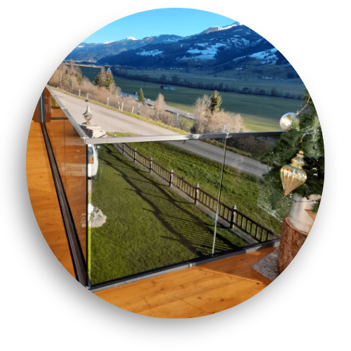 Moderne helglassgjerde uten stolper på terrasse i tre, med åpen utsikt mot landlig natur og snødekte fjell i det fjerne.