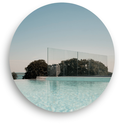 Pfostenloses Glasgeländer am Infinity-Pool mit Fernblick über Baumkronen und Meer – perfekt für offene Terrassen daheim.