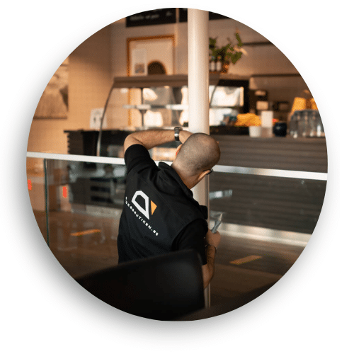 Montør i arbeid med justering av glassrekkverk i en offentlig kantine. Rekkverket består av klart glass og rustfrie detaljer, og gir et stilrent og funksjonelt uttrykk med sikkerhetsklassifisert utførelse.