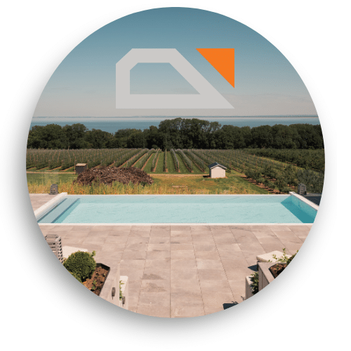 Glassrekkverk gir fri utsikt over åkre og hav fra moderne terrasse ved infinitybasseng – stilrent og sikkert valg.